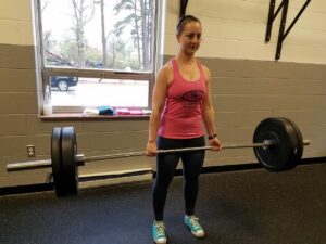 Woman wearing a Glatter Fitness tank top preparing to deadlift a barbell in the gym.